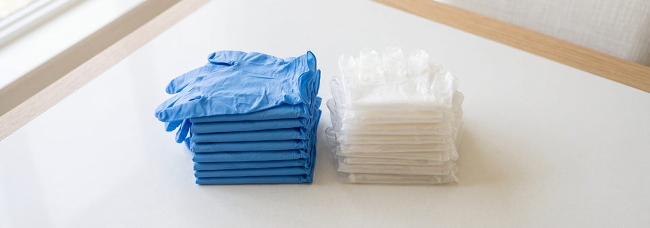 Folded blue nitrile and clear vinyl disposable gloves stacked on a bright surface
